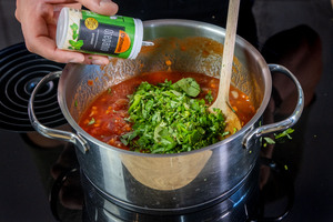 Basilikum und Oregano zur Tomatensauce geben