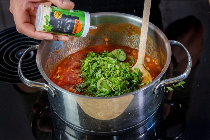 Basilikum und Oregano zur Tomatensauce geben