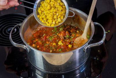 Mais zur Tomatensauce für den Tortellini-Auflauf geben