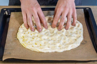 Focaccia-Teig mit Backpulver mit den Fingerspitzen breitziehen