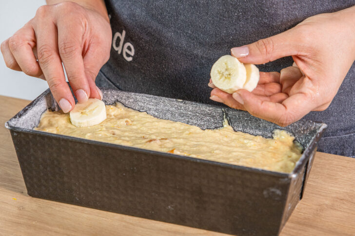 Bananenscheiben in den Teig des saftigen Bananenbrots drücken