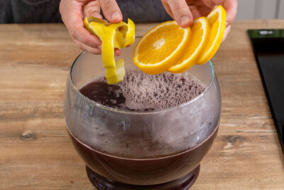 Zitronenschale und Orangenscheiben in die Feuerzangenbowle geben