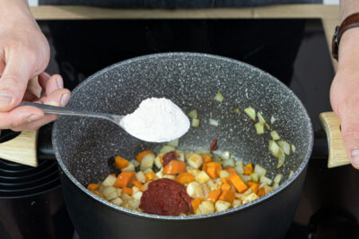 Mehl und Tomatenmark zum Gemüse geben