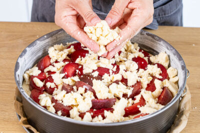 Streusel über dem Pflaumenkuchen verteilen
