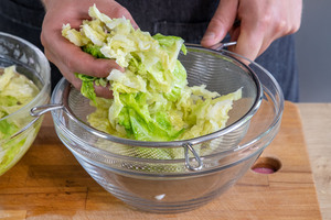 abgeschreckte Wirsingblätter für den Wirsingsalat mit Walnüssen in einem Sieb abtropfen lassen