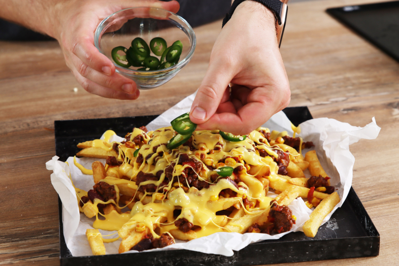 Chili Cheese Fries mit Chilis bestreuen