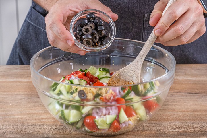 Oliven zum Couscous-Salat mit Feta geben