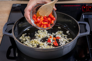 Zwiebel, Knoblauch und Paprikastücke in einer Pfanne glasig dünsten