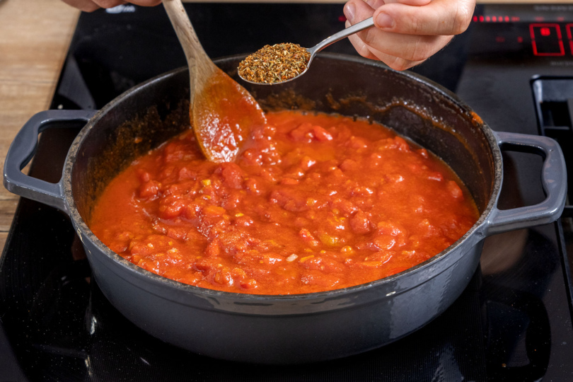 gemischte Kräuter zu der Tomatnsauce für die gefüllten Paprikas geben