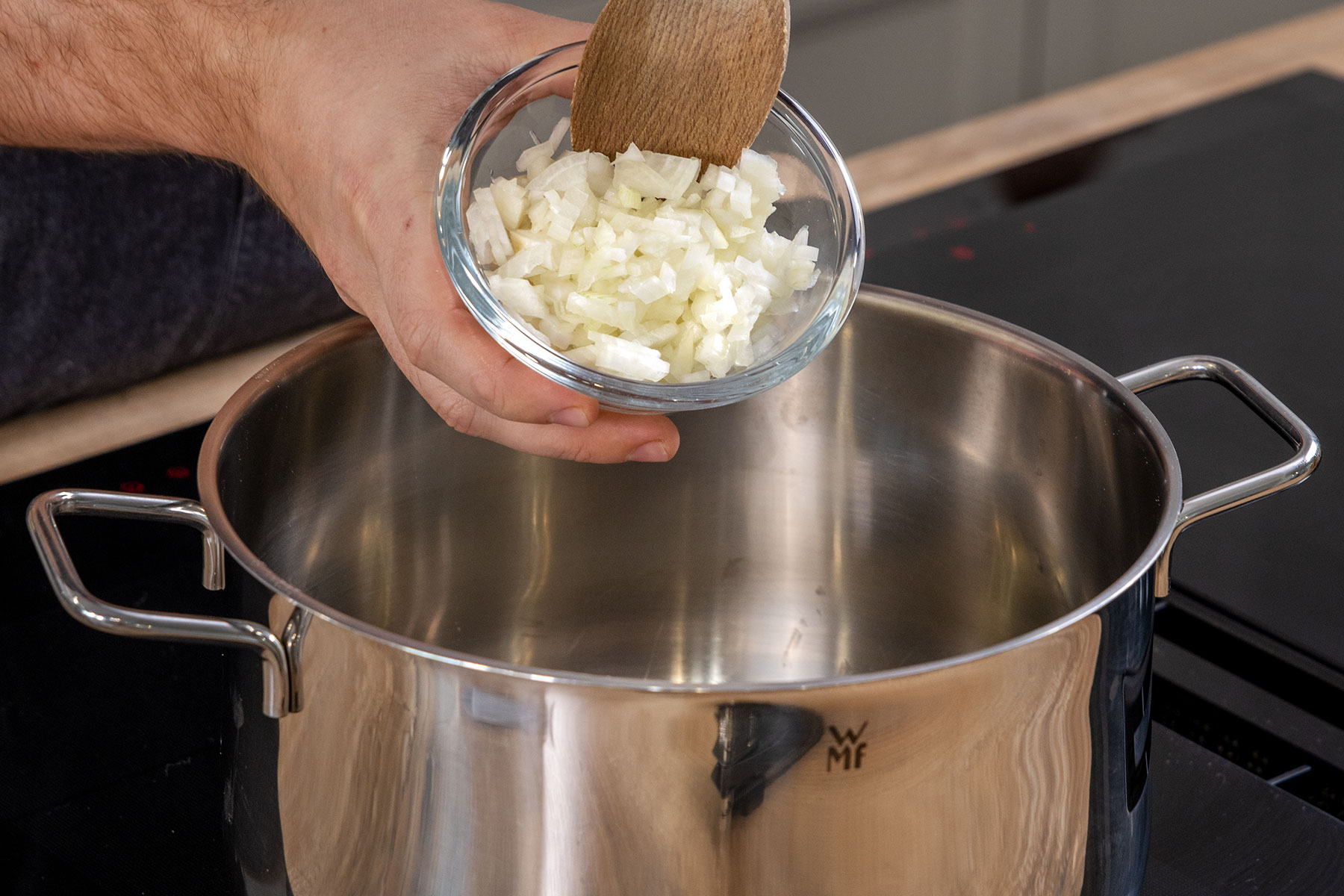 Zwiebelwürfel in den Topf geben