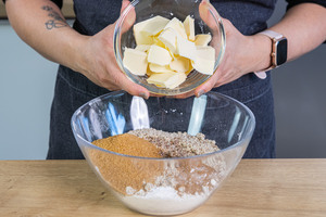 Mehl, gemahlene Haselnüsse, gemahlenen Mandeln, Backpulver, vegane Butter, brauner Zucker, Zimt, Salz, Nelke und Kirschwasser in eine Schüssel geben