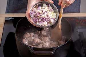 Zwiebel und Knoblauch zu dem Fleisch geben