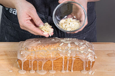 veganen Nusskuchen mit Zuckerguss und gehobelten Mandeln verzieren