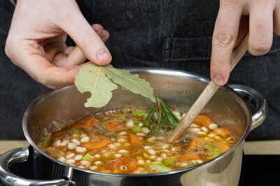 Gewürze und Kräuter in die griechische Bohnensuppe geben