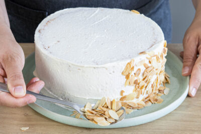 Himbeer-Sahne-Torte mit Sahne einsreichen und die angerösteten Mandelblättchen an die Seite drücken