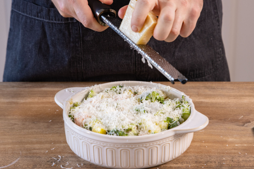 Parmesan über Lachs-Brokkoli-Auflauf reiben