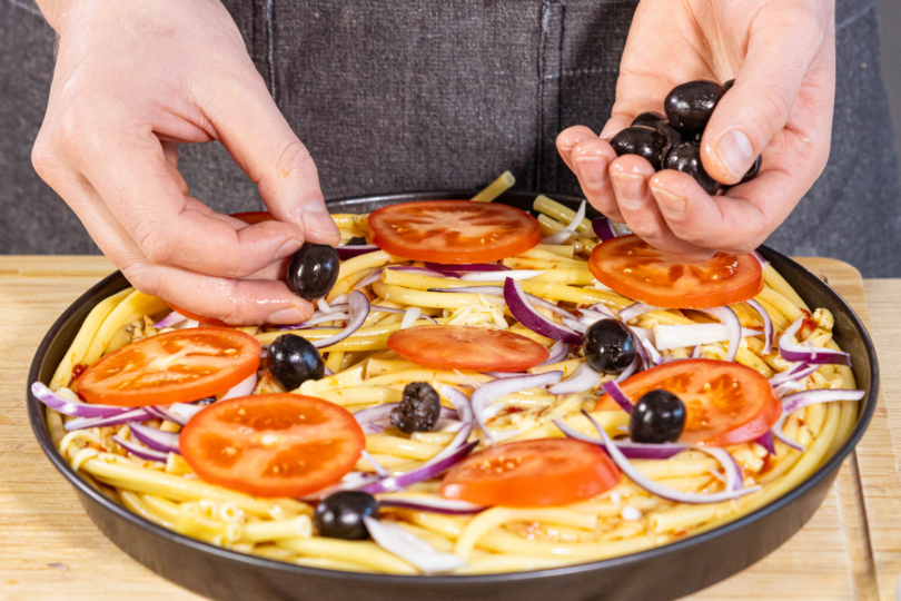 Oliven auf der Nudelpizza verteilen