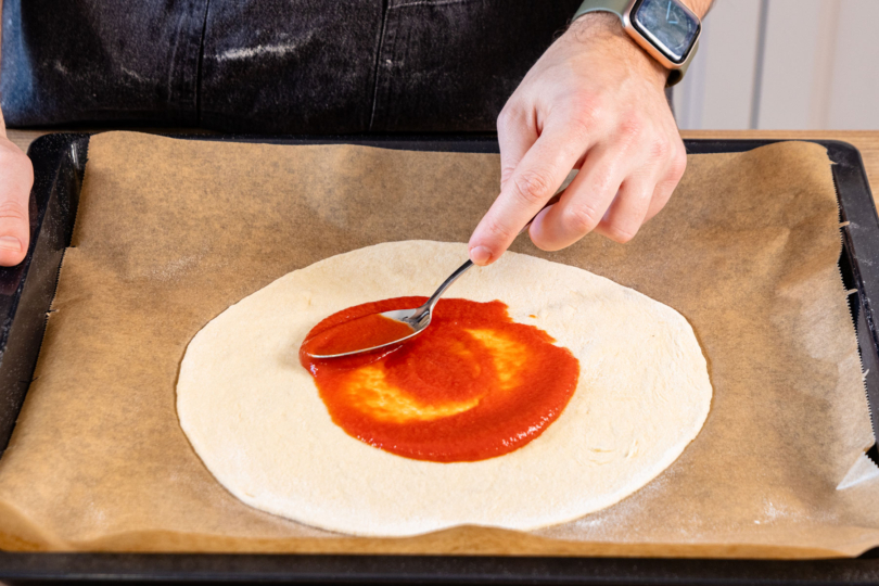 Pizzateig mit Tomatensauce bestreichen.