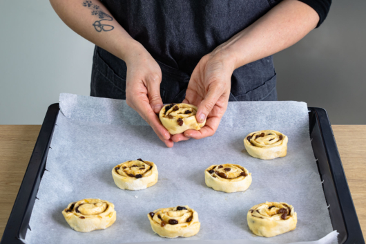 Rohe Rosinenschnecken auf Backblech verteilen