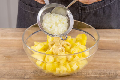Zwiebeln aus dem Sieb zu dem Kartoffelsalat geben
