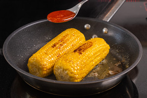 Maiskolben anbraten und Chili-Sauce darüber geben