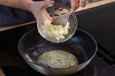 Zwiebeln und Knoblauch in Pfanne geben