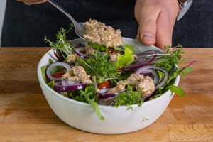 Dressing mit Thunfisch über den Salat geben