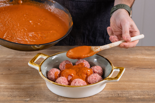 Tomatensoße über Hackbällchen geben