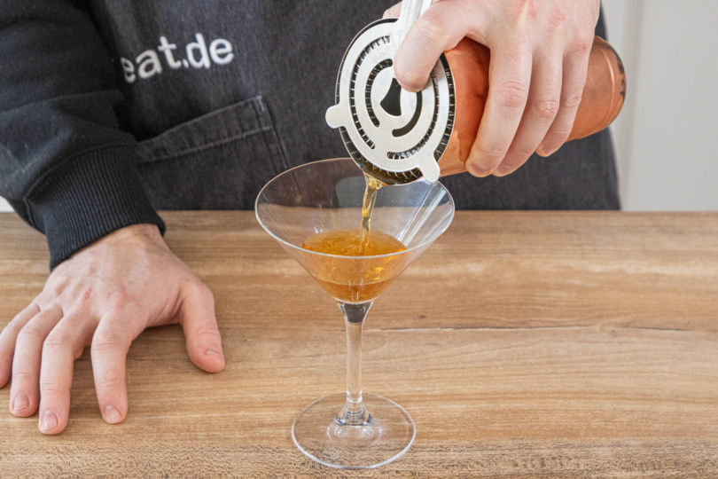 Manhattan Cocktail durch ein Barsieb ins Glas gießen