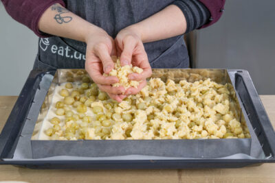 Streusel über dem Stachelbeerkuchen verteilen