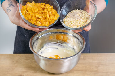 Mandeln und Cornflakes zu der geschmolzenen Schokolade geben