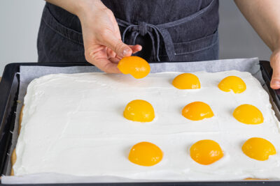 Die Aprikosenhälften auf dem Spiegeleikuchen verteilen
