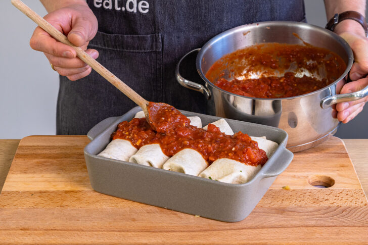 Tomatensoße über vegetarische Enchiladas verteilen