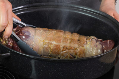 Wildschwein-Rollbraten aus dem Bräter heben