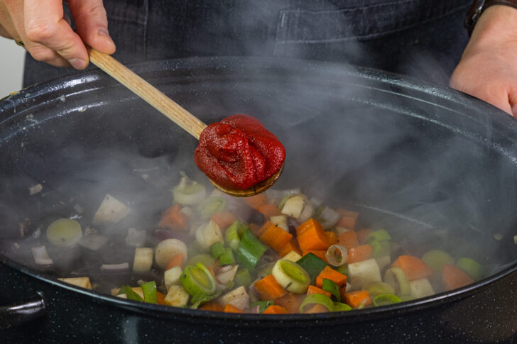 Tomatenmark zu dem Gemüse geben