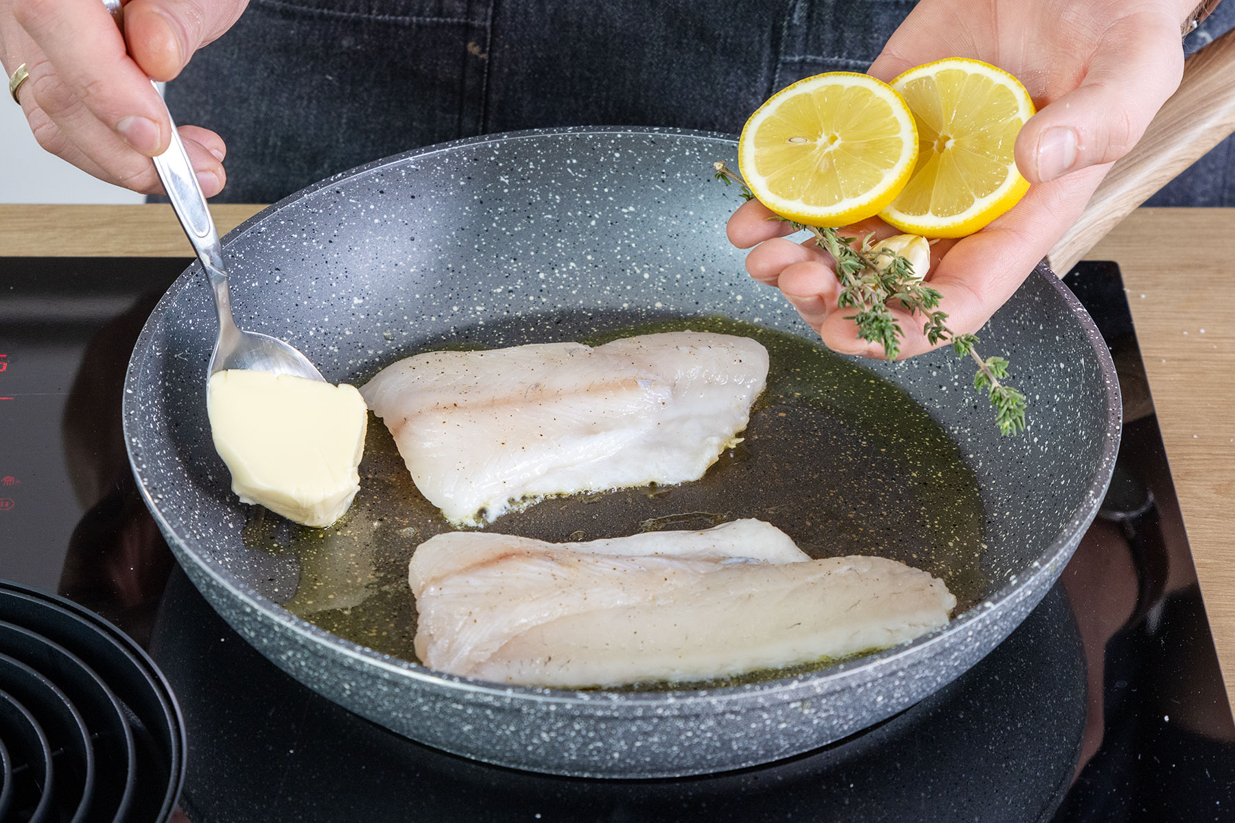 Butter, Zitronenscheiben, Knoblauch und Thymian zu dem Zander in die Pfanne geben
