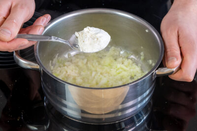 Mehl zu den Zwiebel- und Knoblauchwürfeln in den Topf geben