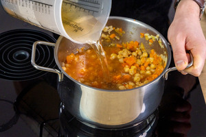 Gemüsebrühe zur Kichererbsensuppe gießen