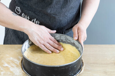 Einen Teil des Streuselteigs als Boden in der Springform verteilen