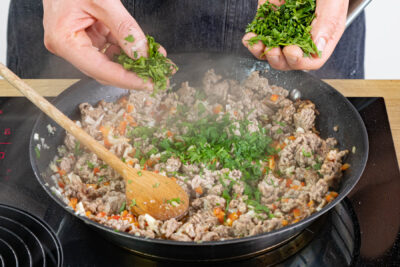 Paprikawürfel und Kräuter zum Hackfleisch geben
