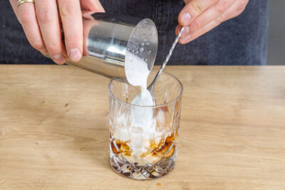 Milch über einen Barlöffel ins Glas gießen