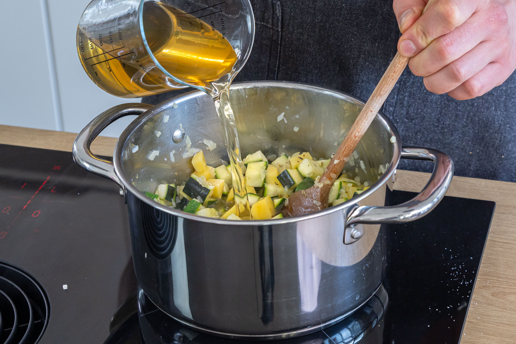 Brühe zur Zucchinisuppe mit Kartoffeln gießen