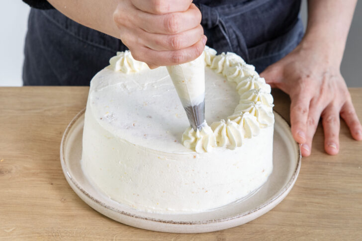 Creme als Tupfen auf den Tortenrand der fruchtigen Mango-Maracuja-Torte spritzen