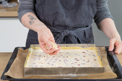 Mandelsplitter über dem Kirschkuchen mit Schmand verteilen