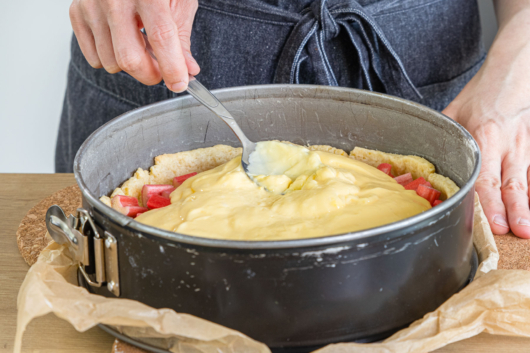 Pudding auf Rhabarberkuchen mit Vanillepudding verteilen