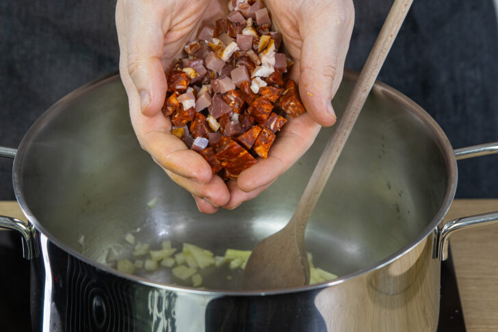 Bauchspeck und Salami in den Topf geben