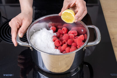 Zitronensaft zur den Himbeeren mit Gelierzucker geben