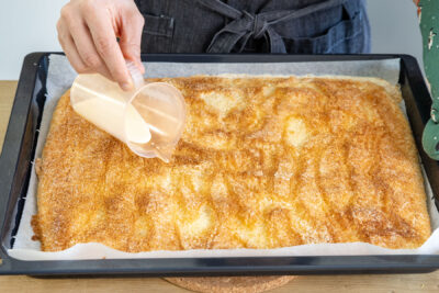 Butter-Sahne-Mischung über den Buttermilch-Kokos-Kuchen geben