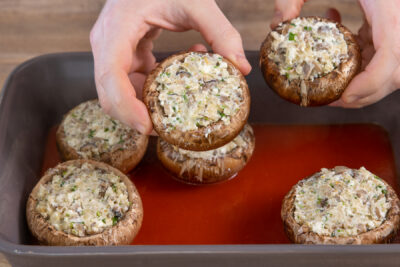 Die gefüllten Champignons mit Feta werden in die Soße gelegt.