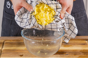 geraspelte Kartoffeln mit einem Geschirrtuch ausdrücken